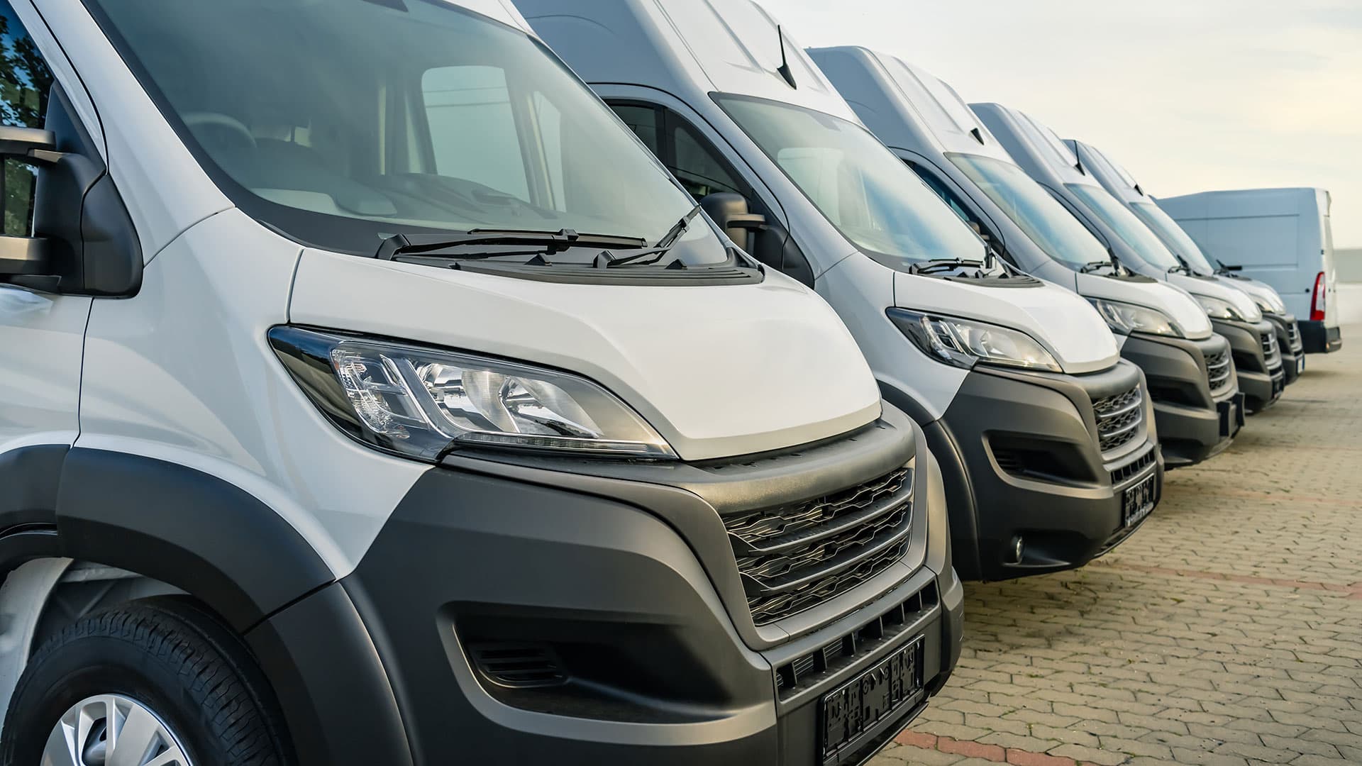 A fleet of new white vans and trucks parked in row outdoors. A fleet of new white vans and trucks parked in row outdoors.