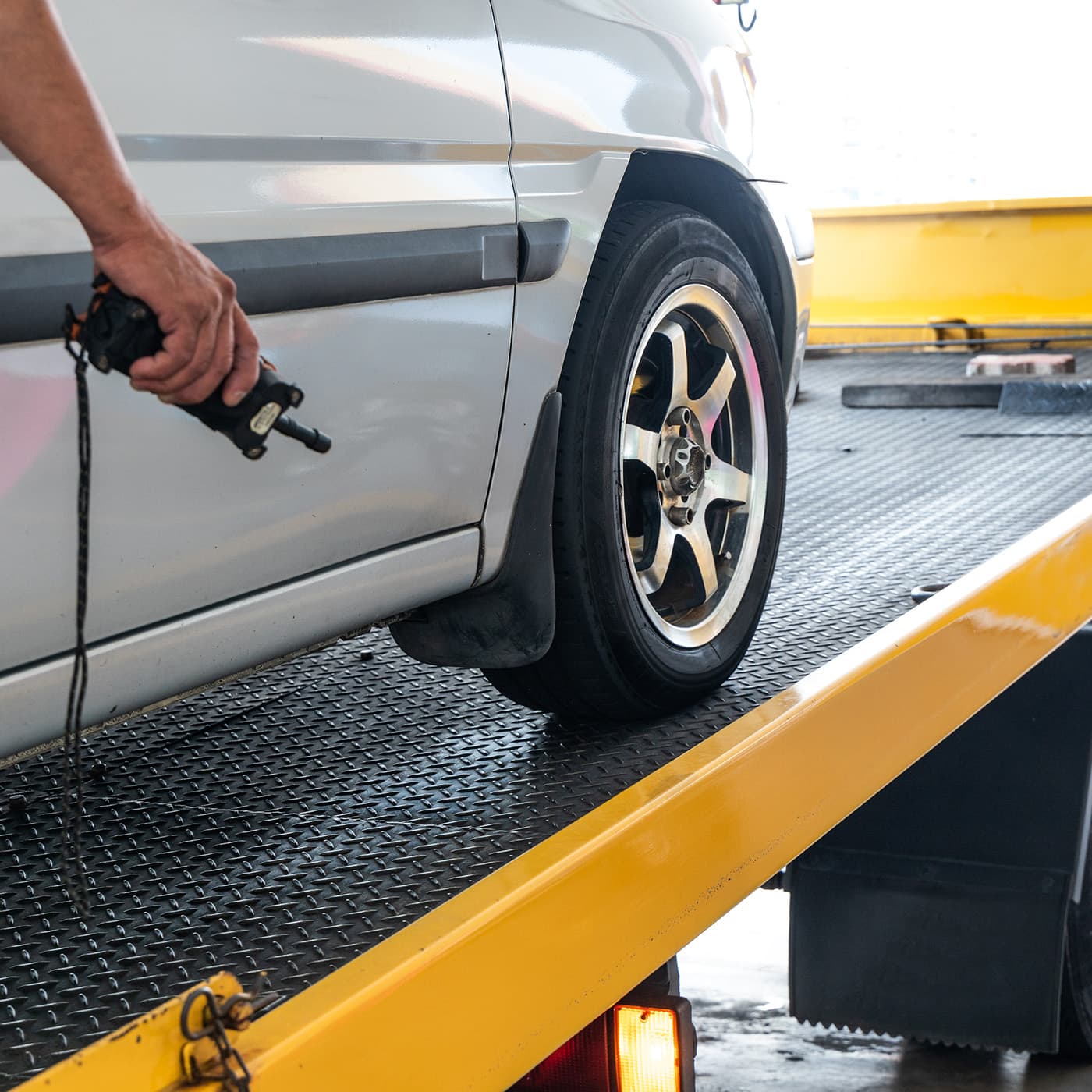 Closeup of broken down car being towed onto flatbed tow truck with cable for repair at workshop garage. Closeup of broken down car being towed onto flatbed tow truck with cable for repair at workshop garage.