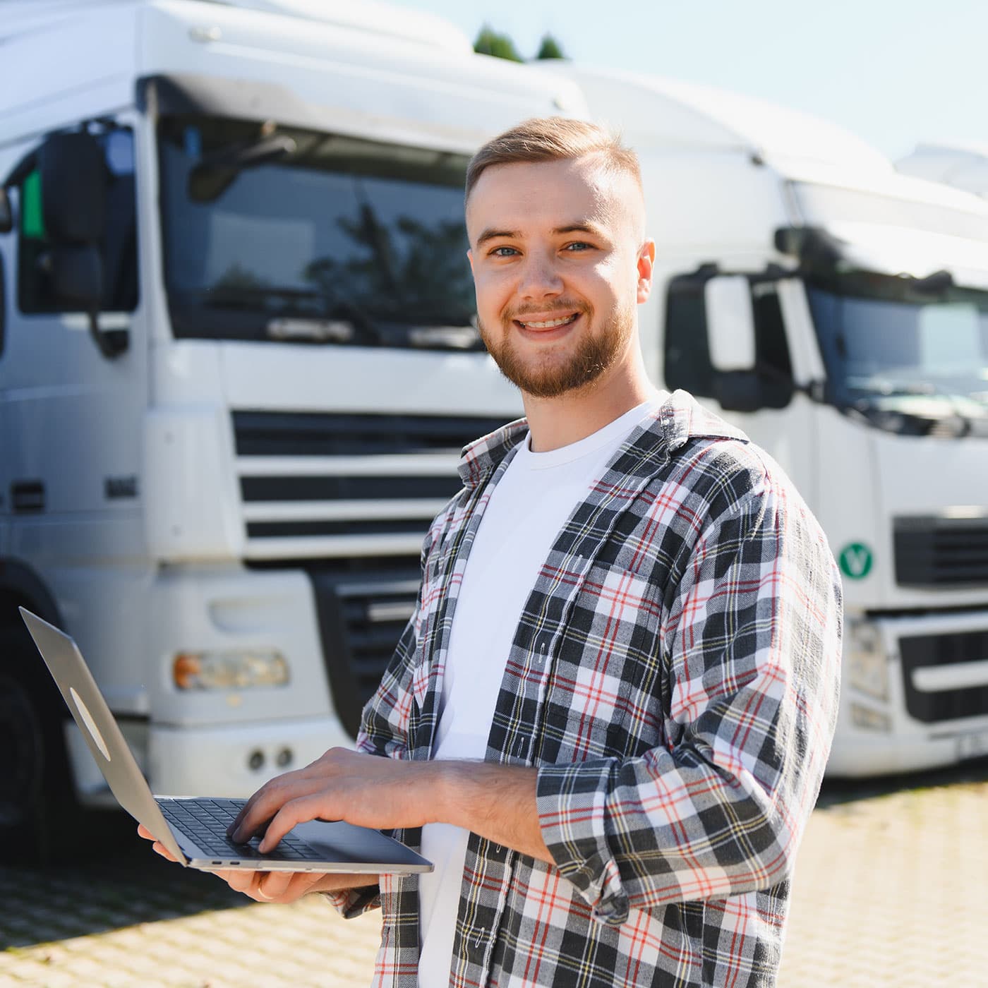 Young business owner holding a laptop, standing outside with a fleet of white trucks in the background. Young business owner holding a laptop, standing outside with a fleet of white trucks in the background.