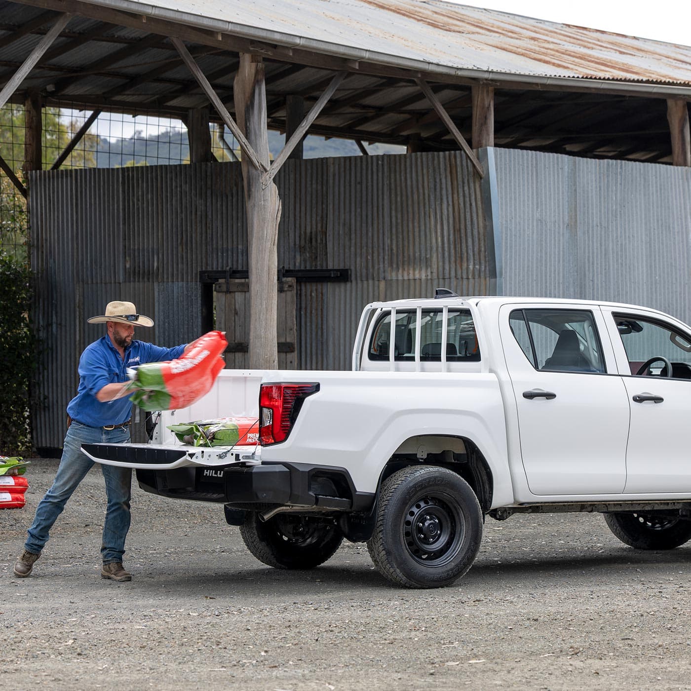 A man in a blue shirt and a hat unloading supplies from a ute. A man in a blue shirt and a hat unloading supplies from a ute.