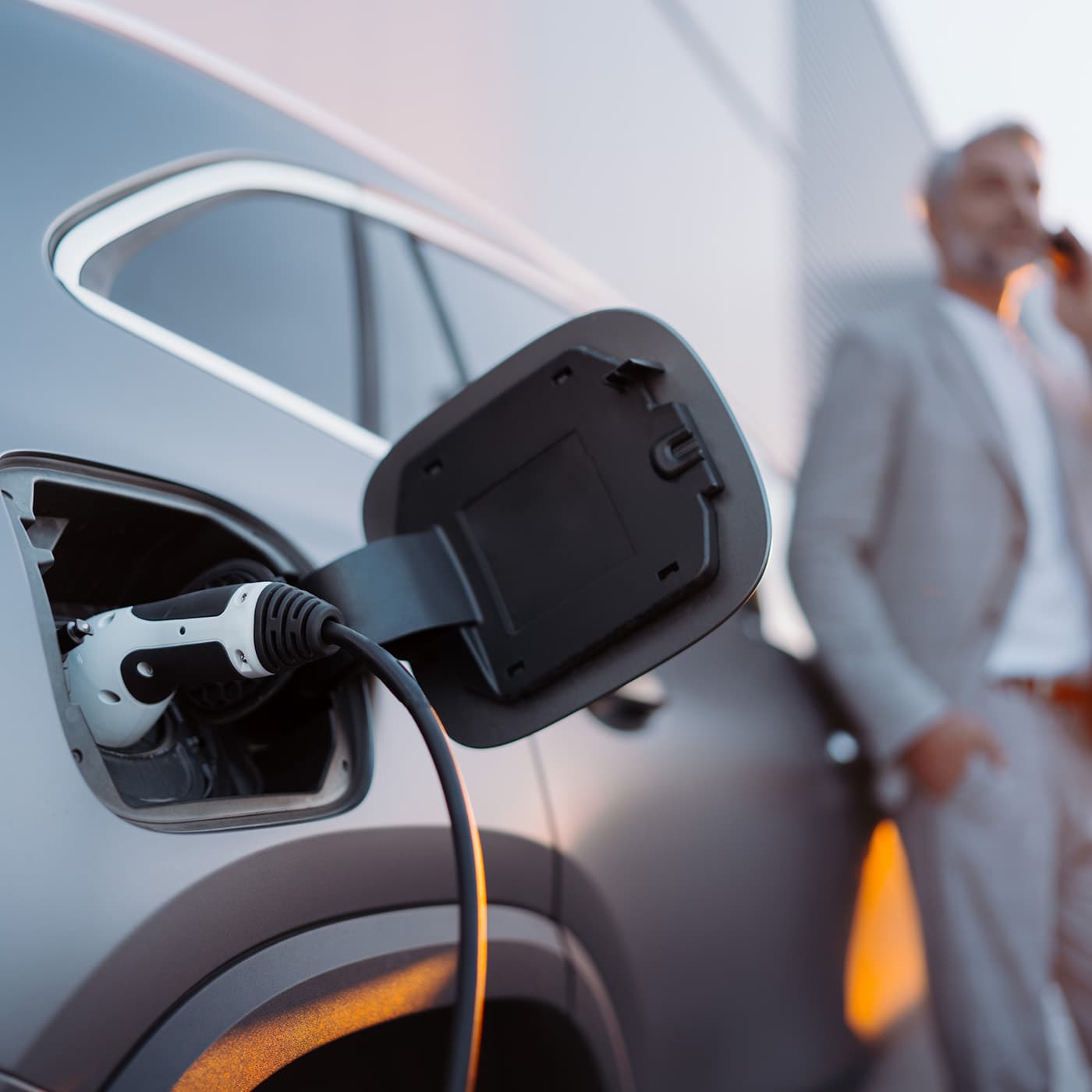 Businessman talking on his phone while charging car at electric vehicle charging station. Businessman talking on his phone while charging car at electric vehicle charging station.