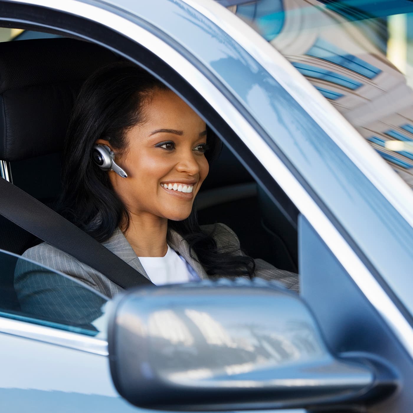 Smiling businesswoman in her blue car wearing a mobile hands-free headset. Smiling businesswoman in her blue car wearing a mobile hands-free headset.