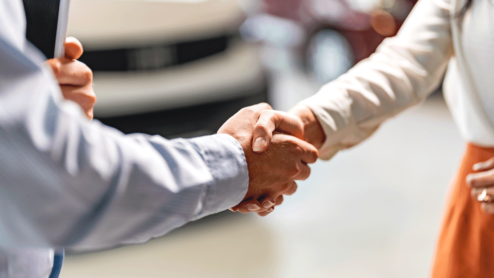 Two people shaking hands beside a car, symbolizing trust, agreement, successful negotiation, customer service, or a vehicle purchase. Two people shaking hands beside a car, symbolizing trust, agreement, successful negotiation, customer service, or a vehicle purchase.