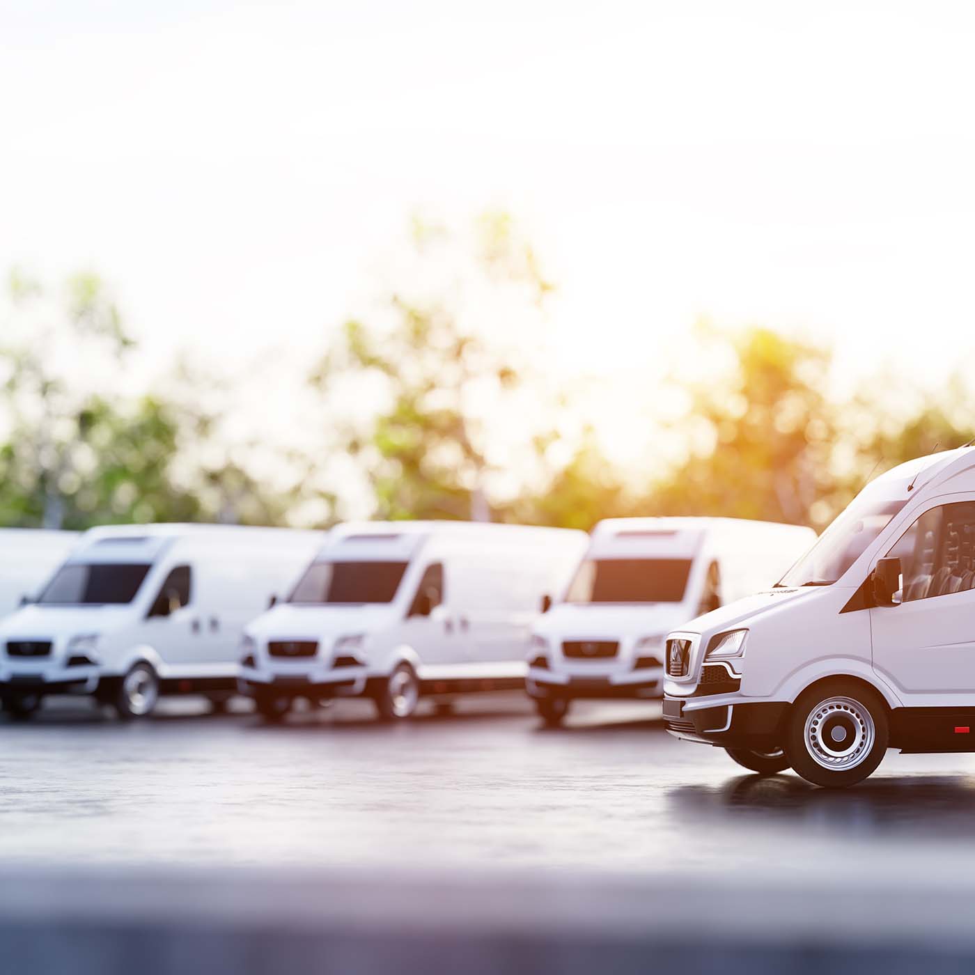 A group of white fleet transportation vans parked outside with trees in the background. A group of white fleet transportation vans parked outside with trees in the background.