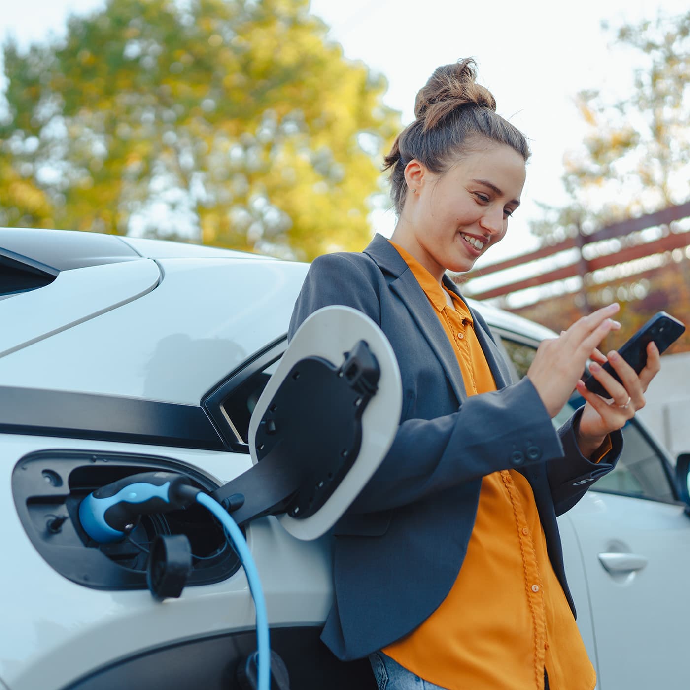 Young woman with smartphone waiting while her electric car charges in her home charging station. Young woman with smartphone waiting while her electric car charges in her home charging station.