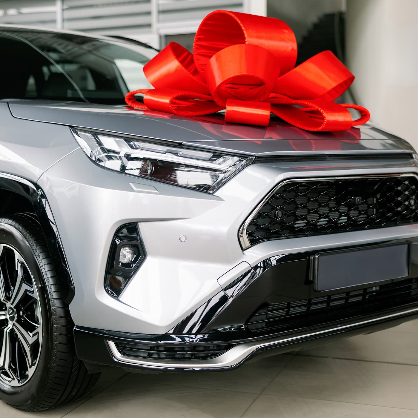 Silver sport utility vehicle decorated with oversized red bow, parked in auto dealership showroom. Silver sport utility vehicle decorated with oversized red bow, parked in auto dealership showroom.