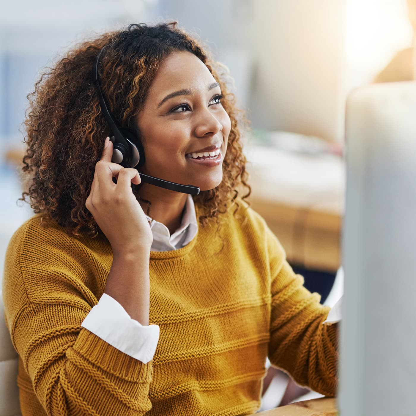Female consultant wearing a yellow jumper and wearing a phone headset, talking to a customer. Female consultant wearing a yellow jumper and wearing a phone headset, talking to a customer.