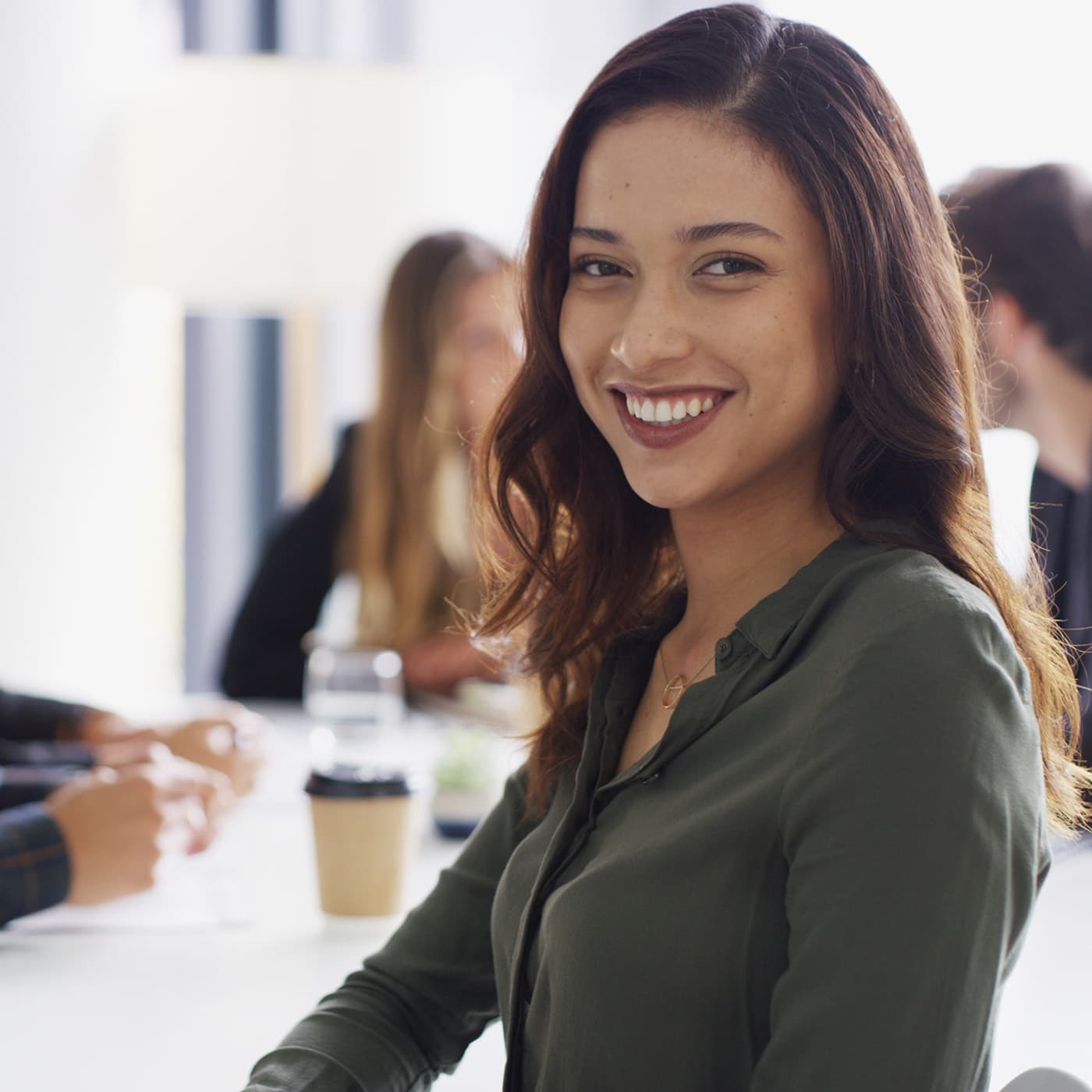 Portrait of a smiling woman in boardroom with other team members in the background. Portrait of a smiling woman in boardroom with other team members in the background.