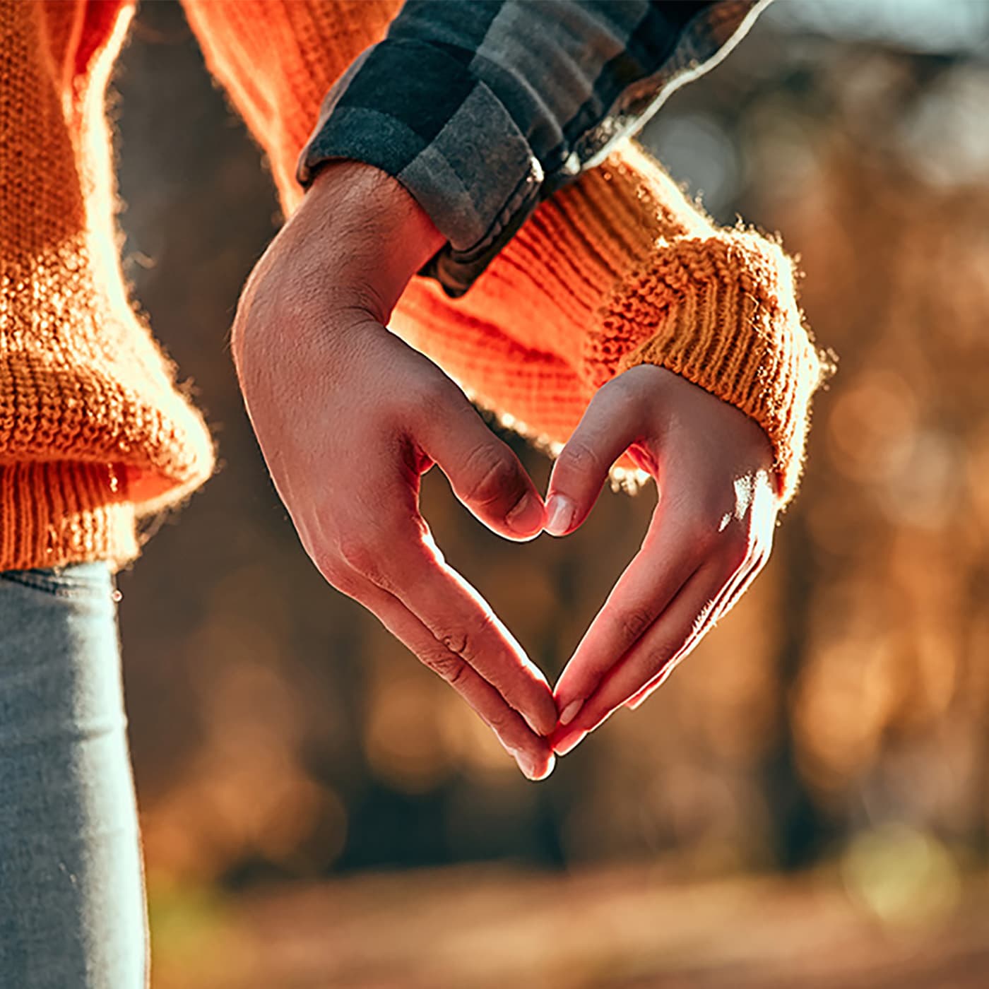 The hero image shows a close up of a man and a woman making the shape of a heart with their hands intertwined. Their lower arms, hands and parts of their torsos are visible only. The woman is wearing blue jeans and an orange sweater. The man is wearing blue jeans and a black and grey checked shirt. The hero image shows a close up of a man and a woman making the shape of a heart with their hands intertwined. Their lower arms, hands and parts of their torsos are visible only. The woman is wearing blue jeans and an orange sweater. The man is wearing blue jeans and a black and grey checked shirt.