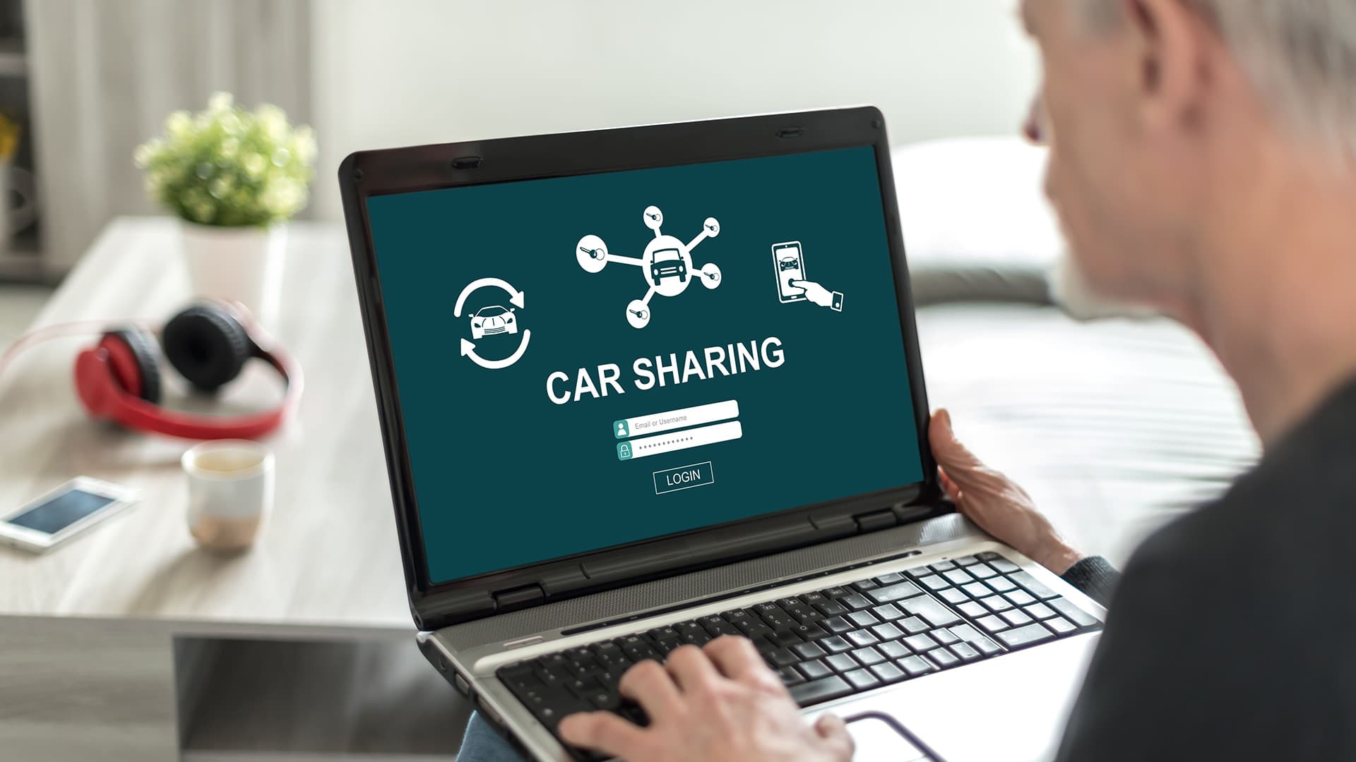 A man sitting in front of a laptop screen displaying a car sharing concept. A man sitting in front of a laptop screen displaying a car sharing concept.