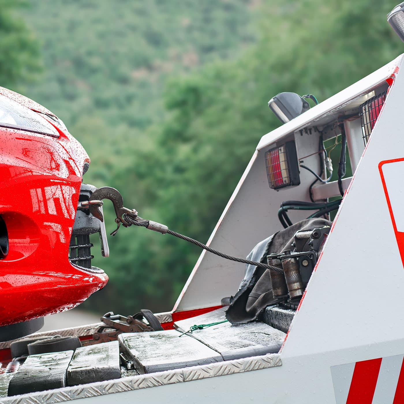 Close-up of a red car being towed by a tow truck on a rainy day with a green forest background. Close-up of a red car being towed by a tow truck on a rainy day with a green forest background.