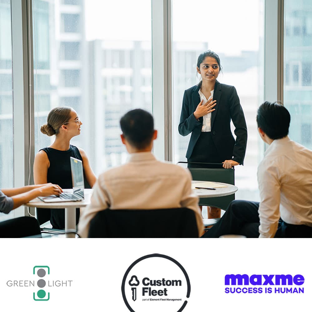 A woman standing up in a meeting and speaking to others in the room. Her hand is on her heart. Green Light, Custom Fleet and MaxMe logos are underneath the photo. A woman standing up in a meeting and speaking to others in the room. Her hand is on her heart. Green Light, Custom Fleet and MaxMe logos are underneath the photo.