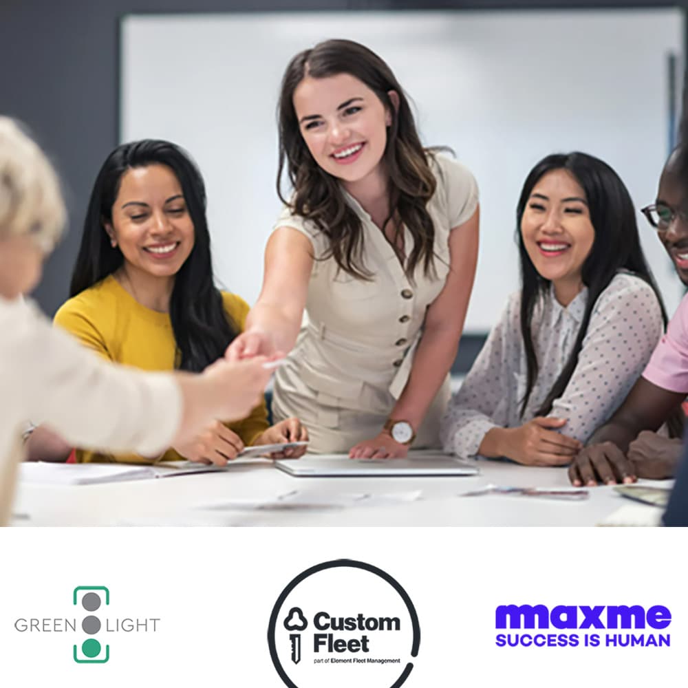A diverse group of professionals, predominantly women, sit around a table engaged in a collaborative workshop. One woman stands and smiles while reaching across the table to shake hands. A diverse group of professionals, predominantly women, sit around a table engaged in a collaborative workshop. One woman stands and smiles while reaching across the table to shake hands.