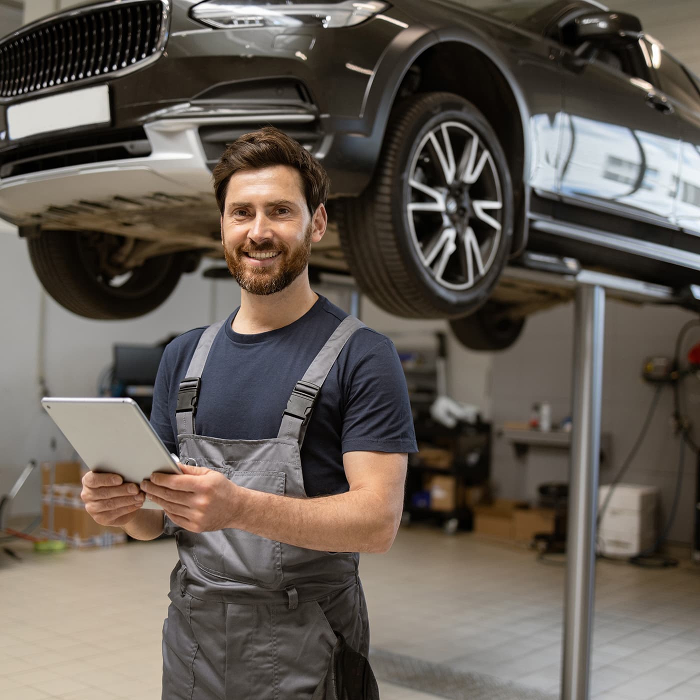 Friendly mechanic using tablet in modern car repair shop with car on lift. Friendly mechanic using tablet in modern car repair shop with car on lift.