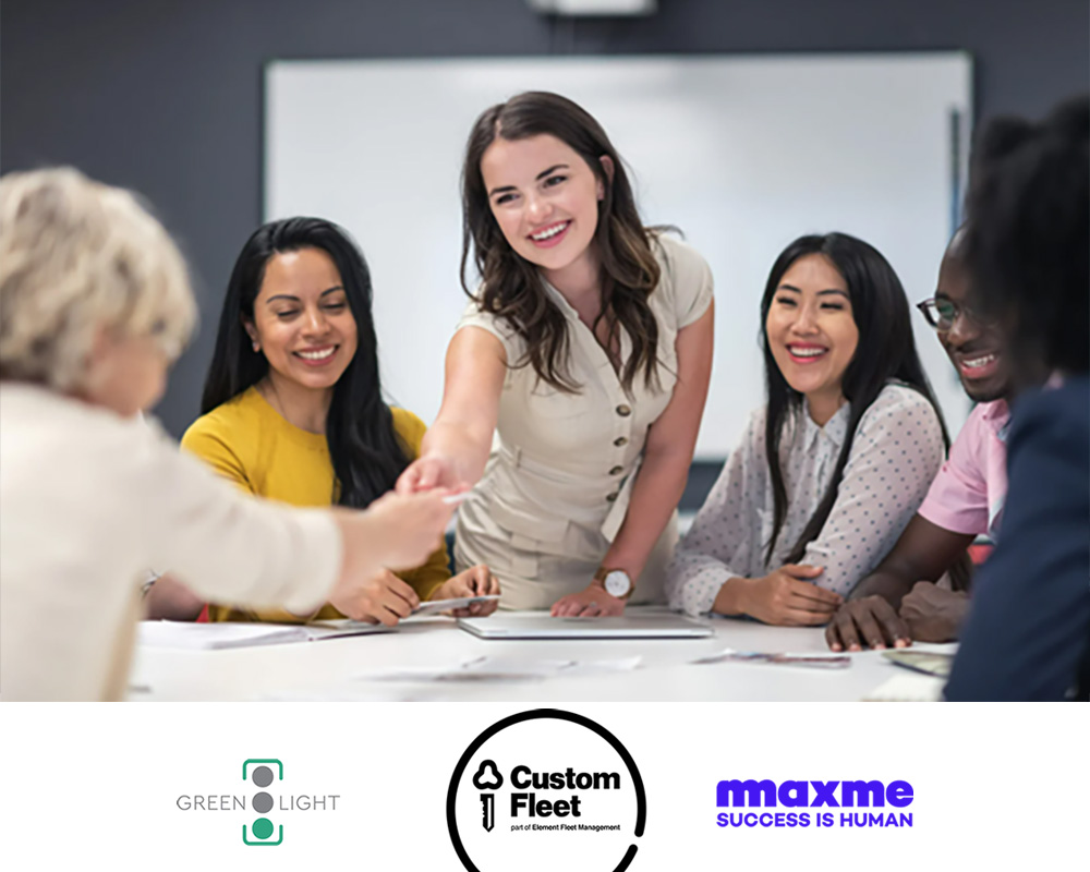 A diverse group of professionals, predominantly women, sit around a table engaged in a collaborative workshop. One woman stands and smiles while reaching across the table to shake hands. Logos for Green Light, Custom Fleet, and Maxme are displayed at the bottom of the image.